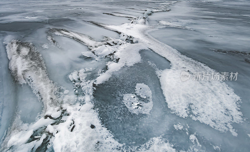 不寻常的动态形状的雪在结冰的湖的破裂冰上漂移，抽象的背景上有一个冬天的湖的裂缝