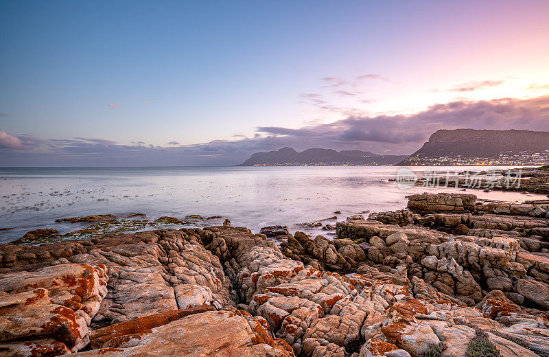 在南非开普敦外的开普半岛的福斯湾，鱼虎克的岩石海岸线上的海浪与充满活力的日落