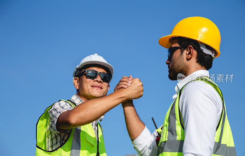 身穿防护工作服的亚洲工程师在蓝色背景上握手的肖像。两个同事在商量合作是否成功。