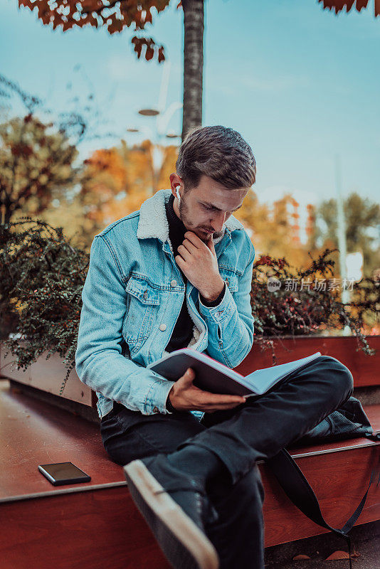 一个学生坐在大学前的公园里看书