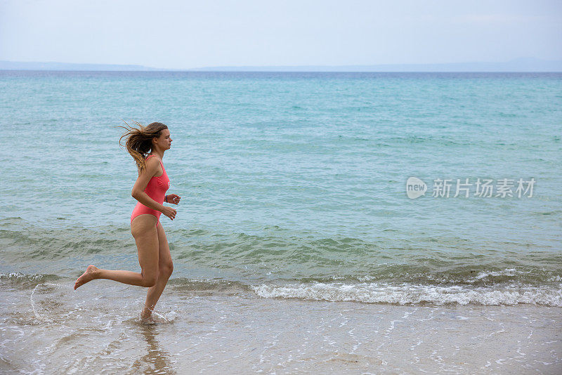 侧视图的年轻女子泳装在海滩上跑步