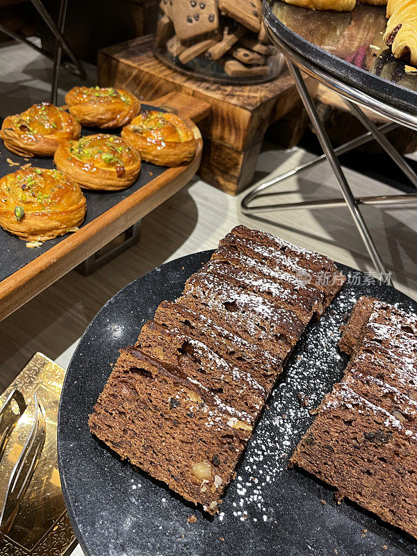 酒店自助餐厅新鲜出炉的早餐蛋糕片，成排的巧克力和核桃海绵蛋糕，丹麦糕点，玻璃饼干罐巧克力片饼干的特写图像，高架视图，重点在前景