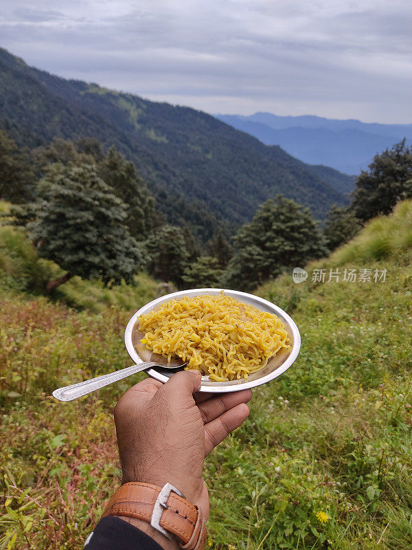 手持盛满面条的盘子，以山为背景的特写镜头