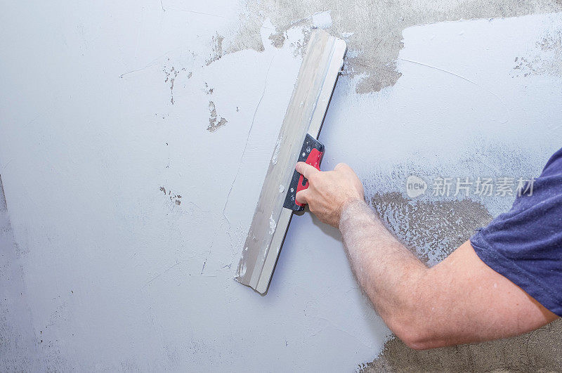 把腻子涂在灰泥墙上。一个男人手拿油漆抹刀的特写。
