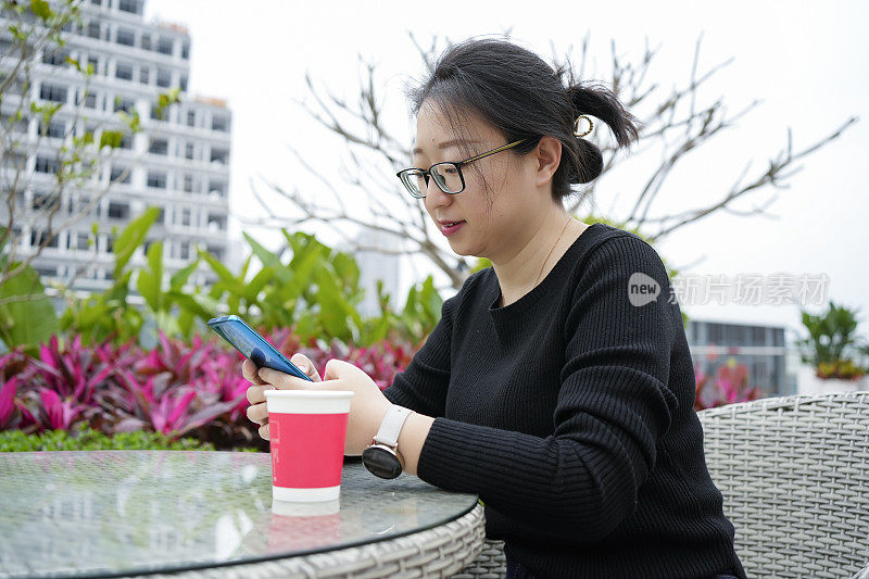 一位年轻女子坐在公园里的藤椅上玩手机