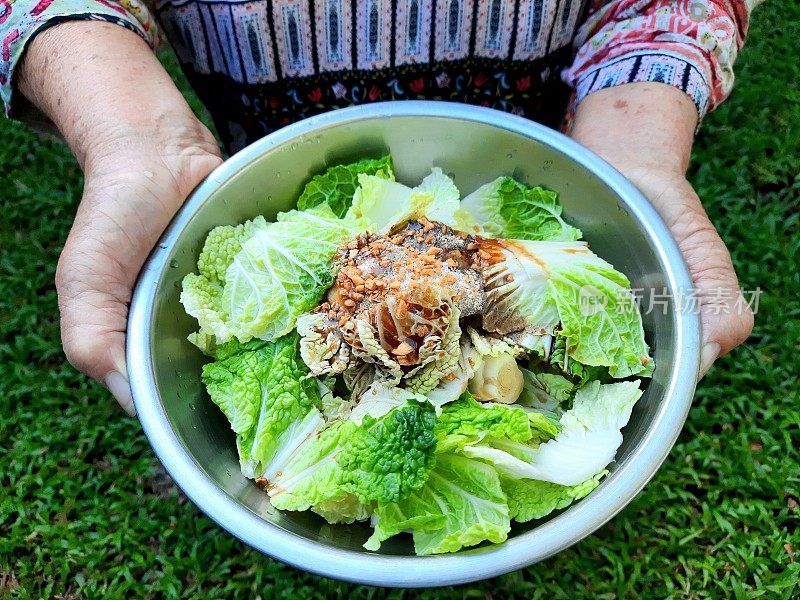 老人手捧一碗准备好的白菜、蔬菜和炒蒜——食物准备。