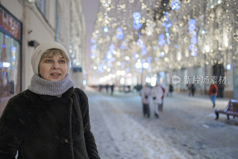 寒假假期。一位迷人的成熟女子，一位旅游者，在圣诞节期间走在灯火通明的街道上，欣赏着为圣诞节和新年假期而装饰的大城市。