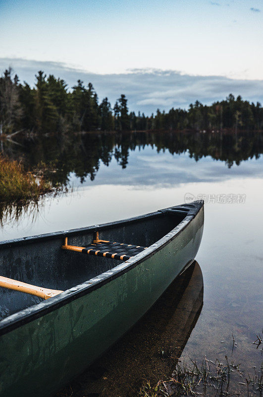 绿色的独木舟停在缅因州树林里宁静的池塘边