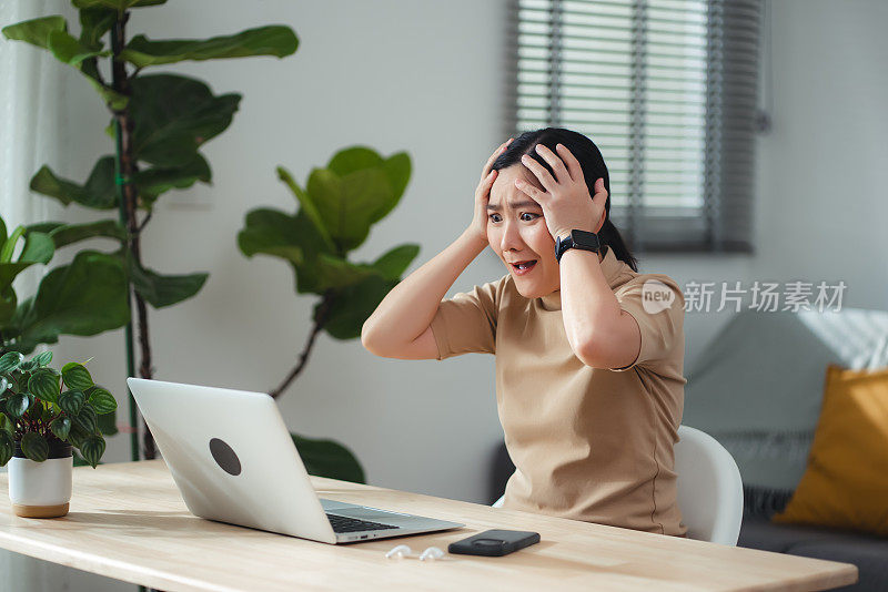 亚洲女性坐在家里的办公室里，看着笔记本电脑，感到震惊和担忧。