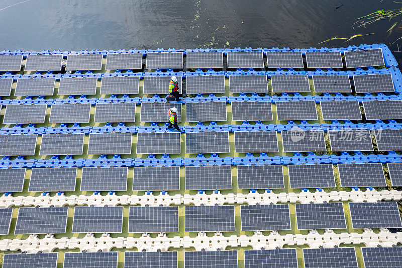 航景或俯视图，两名技术人员沿着太阳能电池板系统从左到右走在水库上，为绿色生态系统提供能源，营造良好的环境。