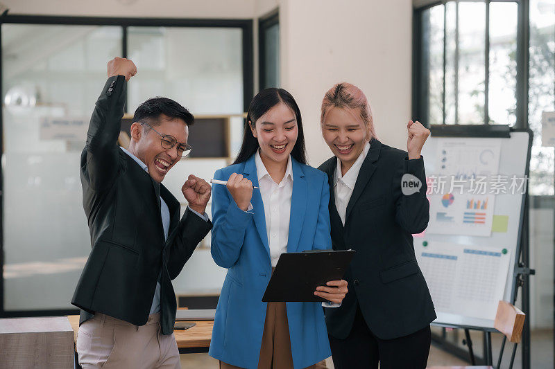 快乐的亚洲商业团队在办公室高举双手庆祝成功。企业胜利和团队成就的理念。