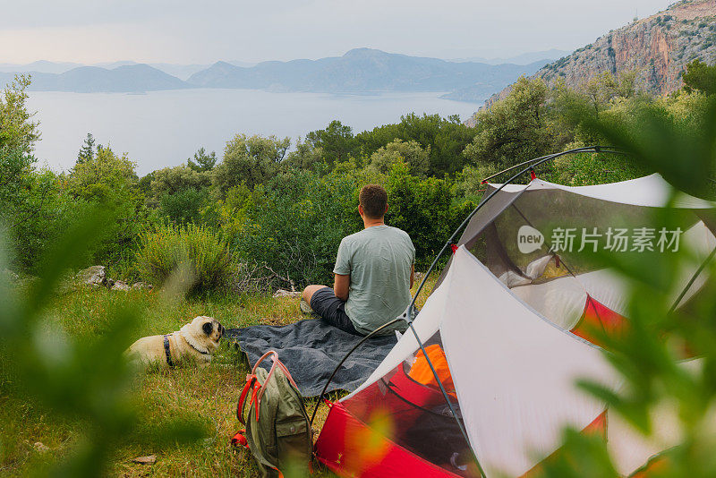 在土耳其，一个人带着狗在眺望日落露营的海景