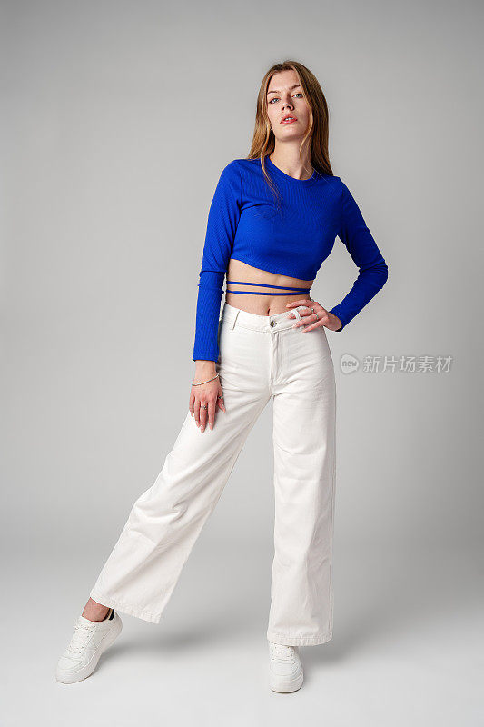 年轻女子模特在蓝色上衣和白色裤子摆姿势在白色背景