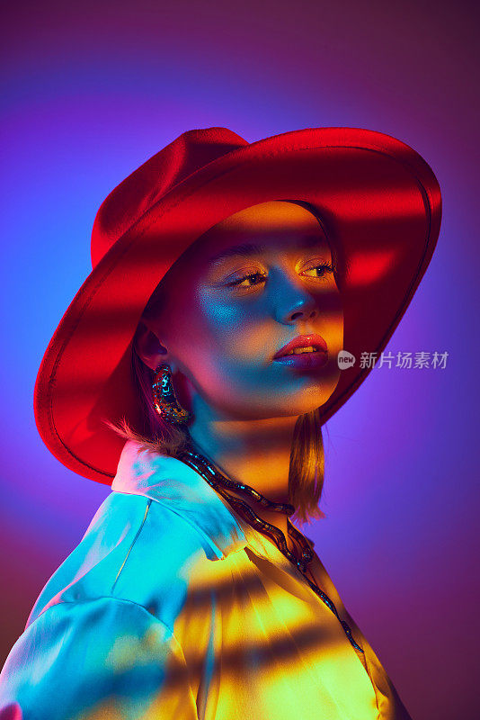 动态时尚肖像的女人在充满活力的红色帽子，与冷暖霓虹灯对渐变紫色背景的相互作用。