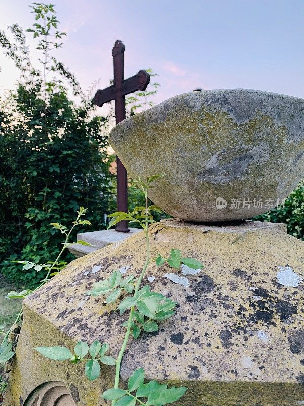 古老的风化石碗在墓碑上，十字架在背景