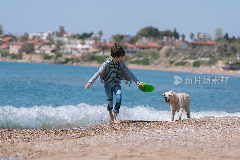 快乐的男孩和她的狗在沙滩上奔跑