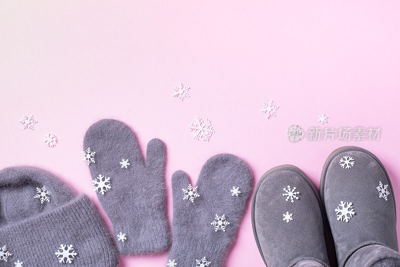 冬天暖和的衣服平躺着。羊毛女性服装毛衣，围巾，靴子，粉红色背景的雪花。俯视图，复制空间