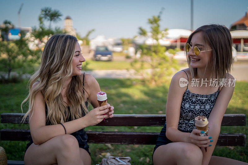 两个美丽的女孩在夏日公园散步，最后聊了起来。朋友们穿着时髦的衬衫和牛仔裤短裤，享受着休息日的乐趣。