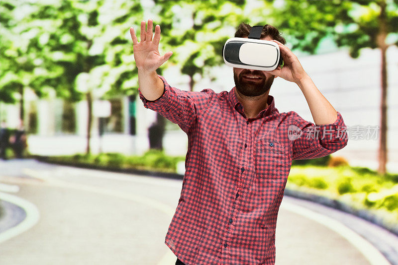 白种年轻男性在室外使用虚拟现实模拟器的散焦背景前