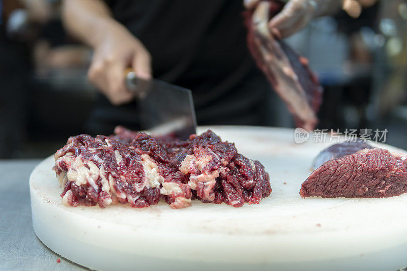 在一家牛肉火锅餐厅的开放式厨房里，厨师正在用刀切牛肉