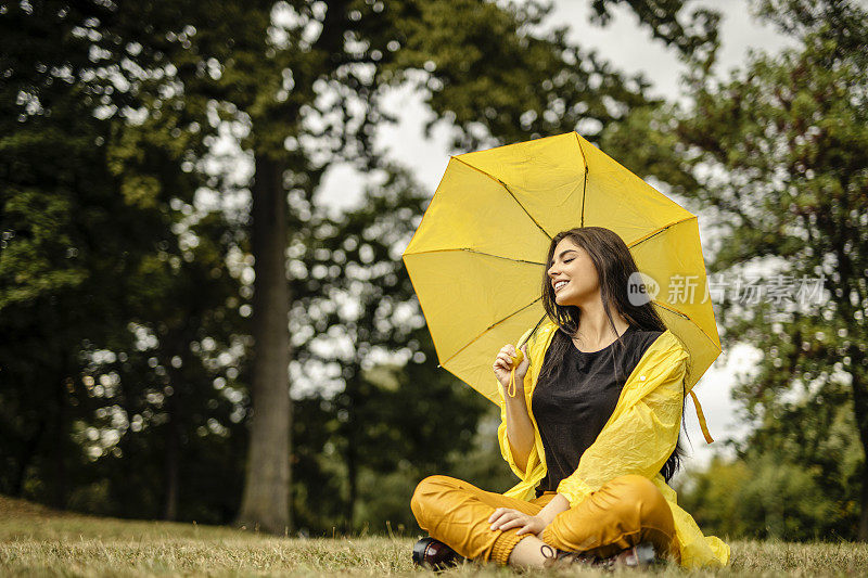 美丽的年轻女子穿着黄色雨衣，拿着黄色雨伞在户外