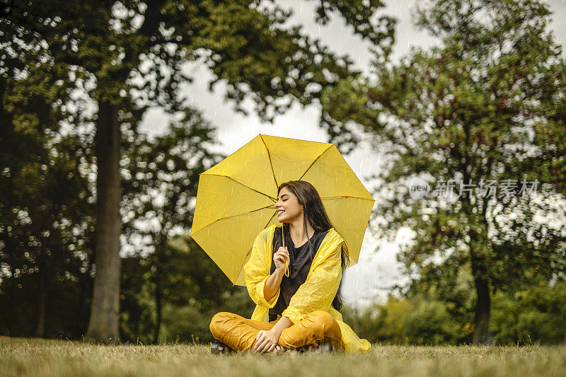 美丽的年轻女子穿着黄色雨衣，拿着黄色雨伞在户外