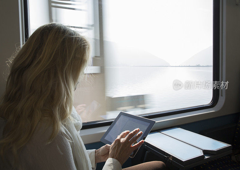 一名女子在湖上乘坐火车时使用平板电脑