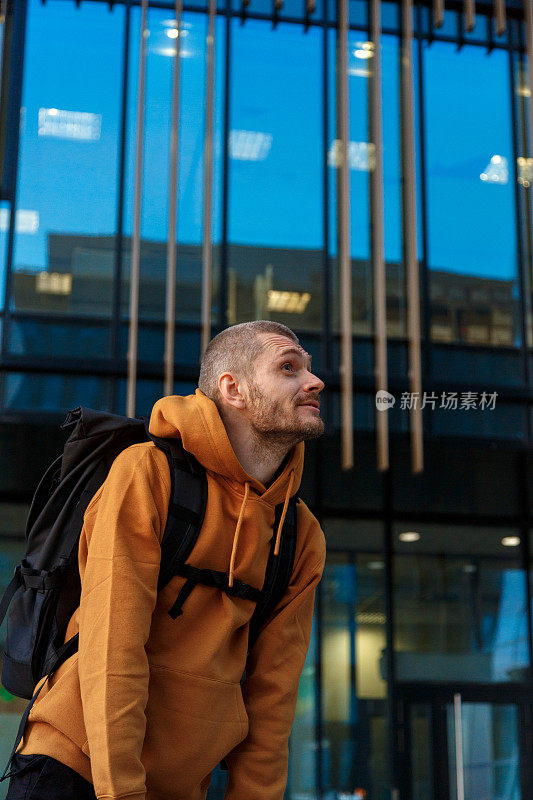 一名身穿鲜红色连帽衫的男子骑着自行车穿过城市中现代化的玻璃建筑