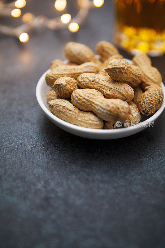 花生在一个小盘子上，在一个黑暗的表面与一杯啤酒和派对串灯，并复制空间