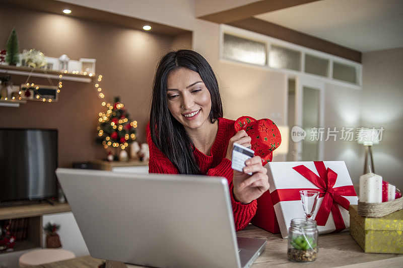 女人用信用卡在家里买新年的礼物-圣诞购物-一个年轻女人在网上买礼物的特写