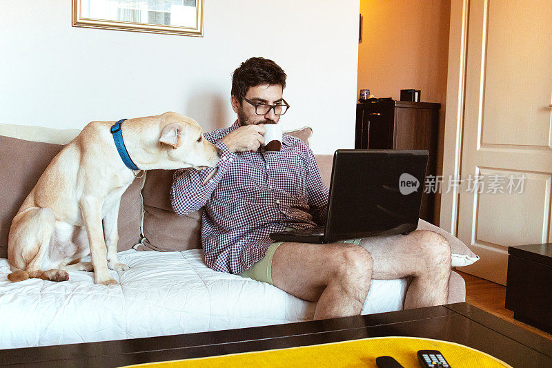一个年轻人和他的狗坐在客厅的沙发上，用着笔记本电脑