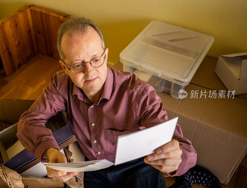 中年白人男子在空的公寓房间里，从纸箱里取出行李准备搬家