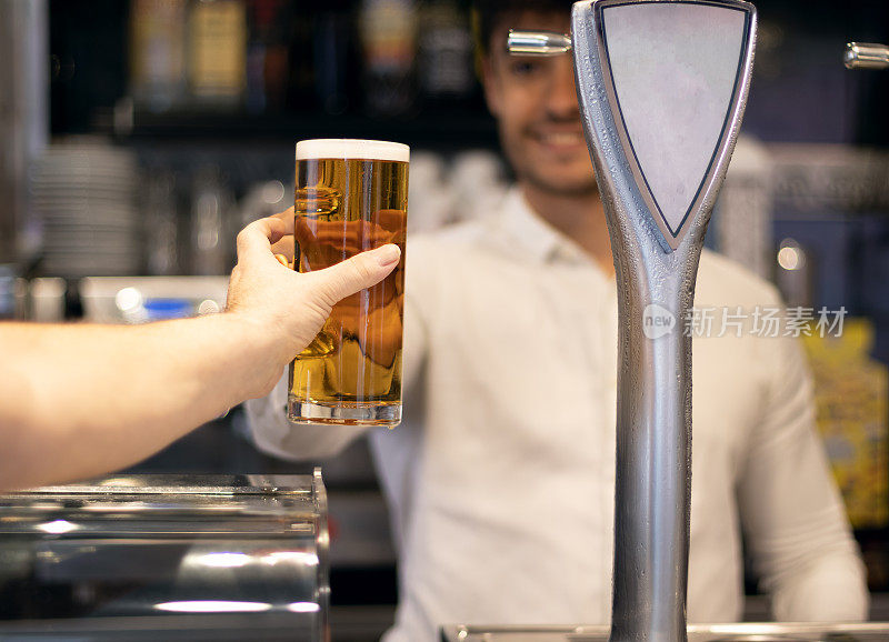在酒吧里，酒保微笑着给顾客一罐啤酒。