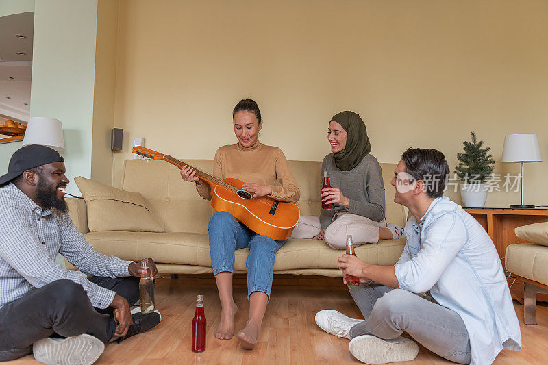 欢乐的多民族朋友们在现代公寓里放松，弹着原声吉他。