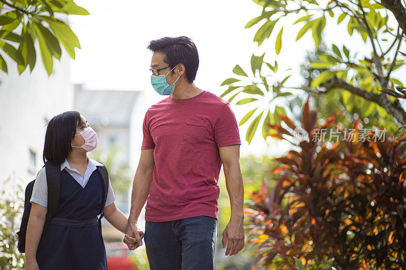 亚洲华人单身父亲和女儿戴着口罩一起在公园散步回学校