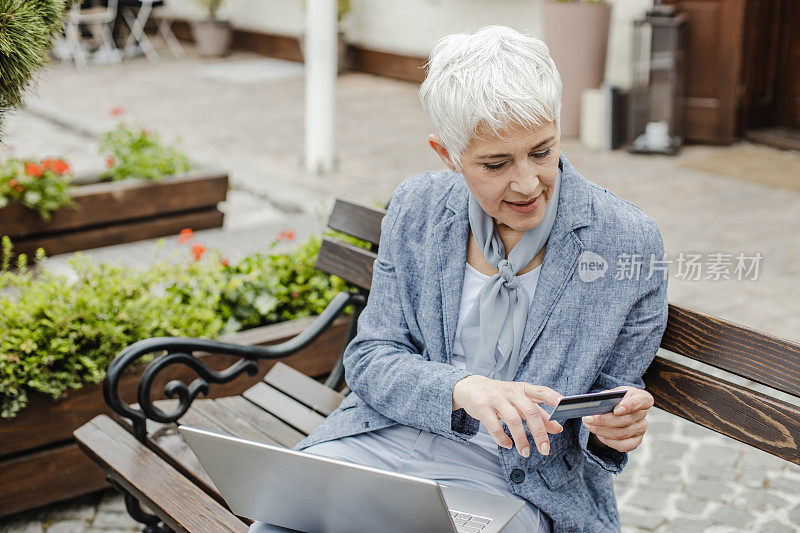 一个成熟的女人在街上用笔记本电脑在网上购物