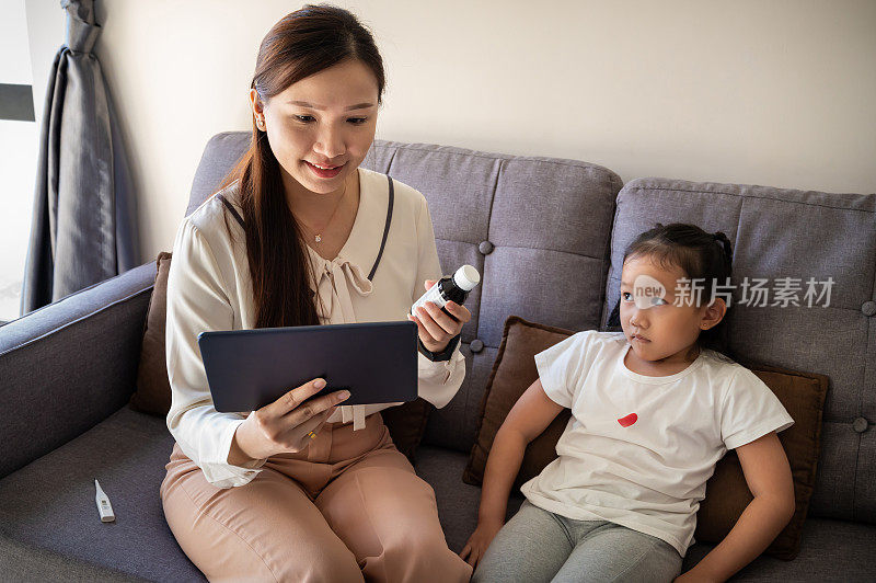 年轻的亚洲母亲咨询医生对她的女儿的咳嗽和流感处方药物使用数字平板在客厅。