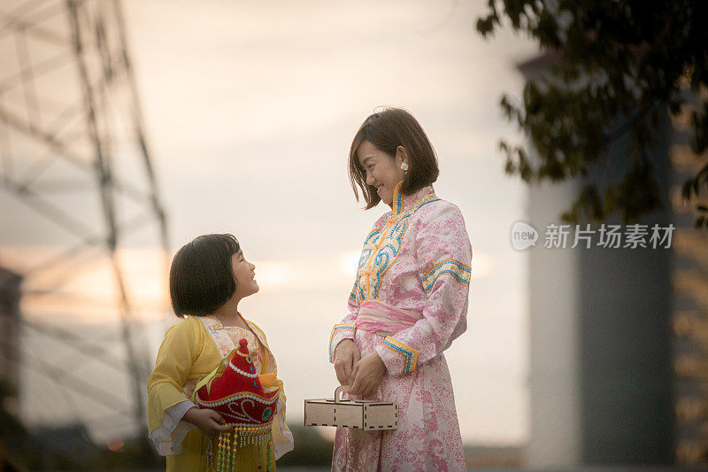 亚洲华人妈妈和女儿穿着传统服装，手拿月饼盒享受月饼节