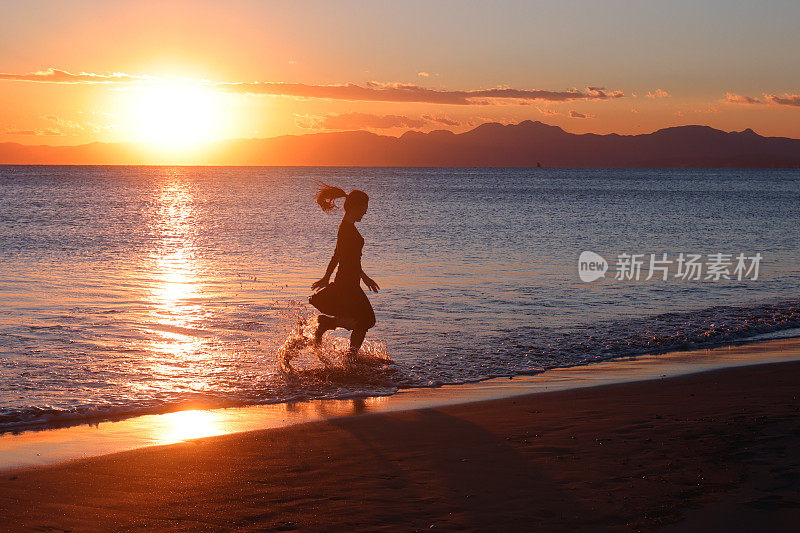 美丽的年轻女子在日落的海滩上奔跑