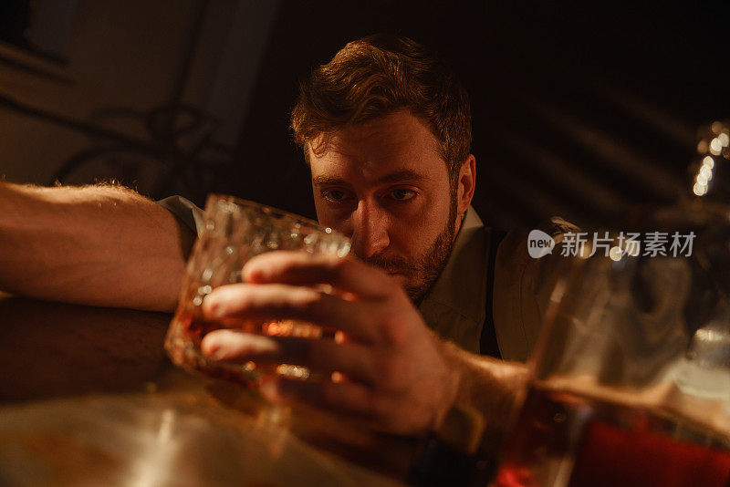 餐桌上一个喝着威士忌的醉汉的大气肖像。一个醉酒的男人看着手里拿着的一杯威士忌。