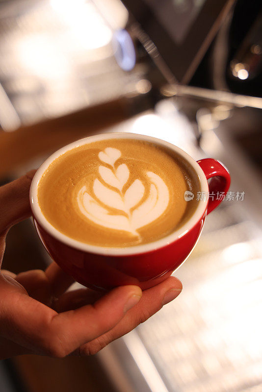 咖啡师端上的拿铁在牛奶泡沫上有花朵图案