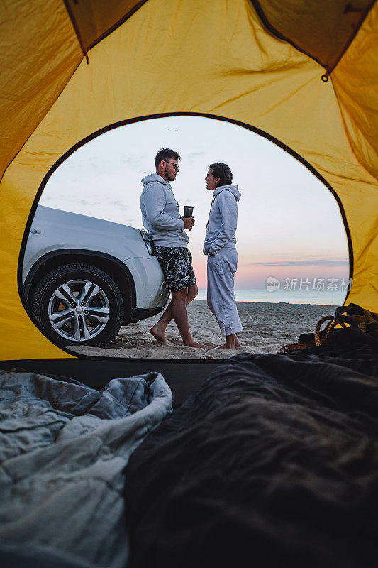 情侣在海边日出相遇。透过露营帐篷看风景