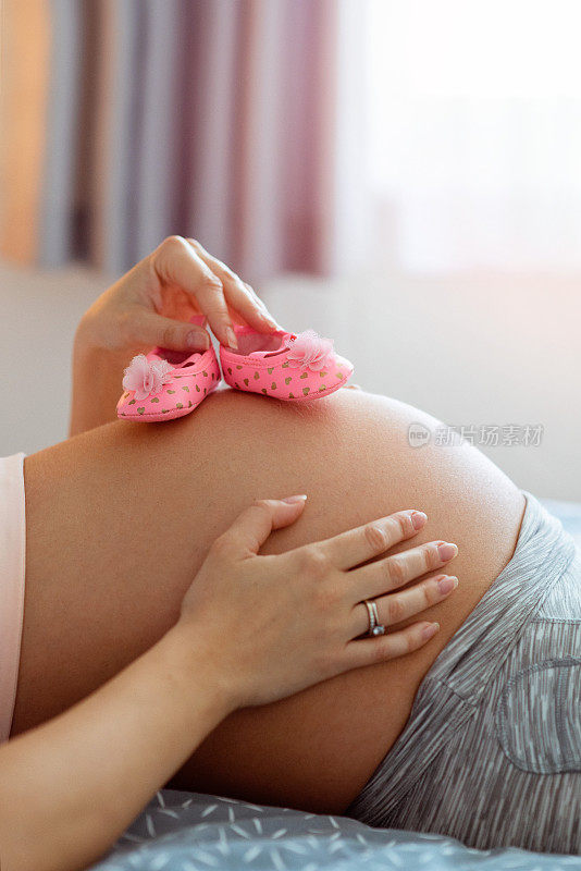 穿着粉红色婴儿鞋露出肚子的孕妇