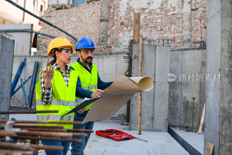 一名女建筑工人和她的同事在建筑工地上戴着防护头盔，穿着反光服