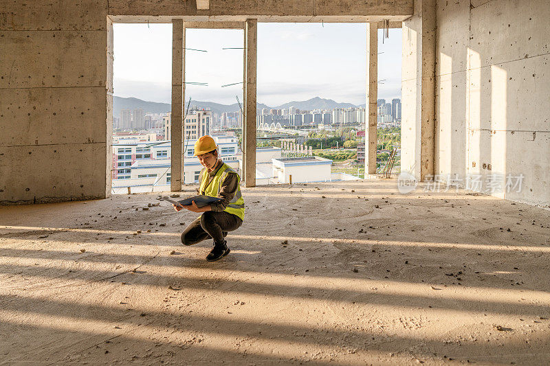 一位亚裔女工程师蹲在建筑工地的地板上看图纸