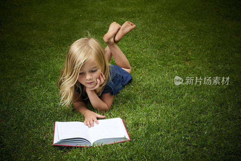 可爱的金发小女孩在外面看书