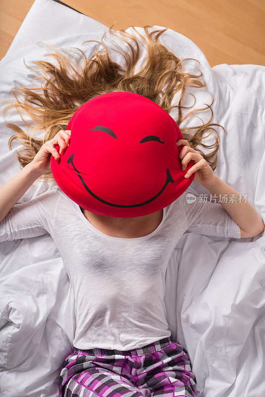 一个女人用一个笑脸形状的枕头遮住脸