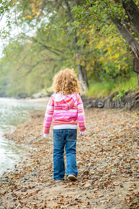 年轻女孩沿着河岸行走的后视图