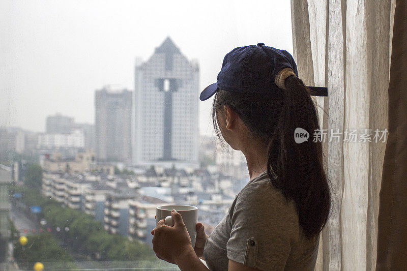 女孩站在窗边，俯瞰城市风光