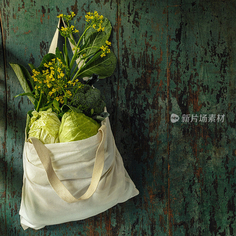 健康新鲜的绿叶蔬菜挂在一个可复苏的天然棉花购物袋里，挂在破旧的乡村木板上的生锈钉子上。